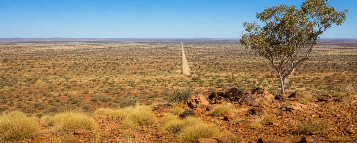 Vidsträckt rödjordsslätt i centrala Australien med en rak grusväg mot horisonten